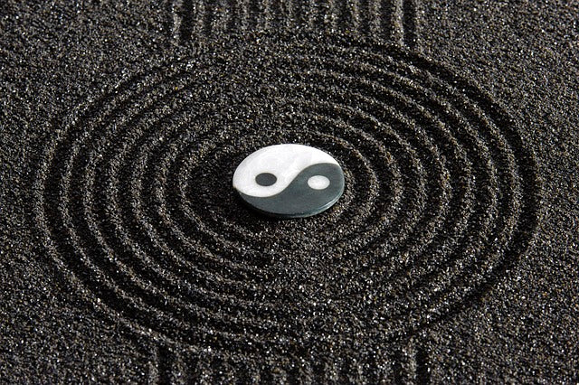 yin and yang token in black sand